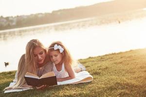 mamma med ett barn läser en bok på gräset foto