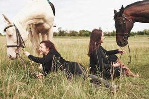 två unga vackra tjejer i redskap för ridning nära sina hästar. de älskar djur
