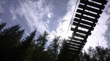 botten se av man på suspension bro. stock antal fot. man promenader på trä- suspension bro på bakgrund av gran blast och blå himmel med Sol foto