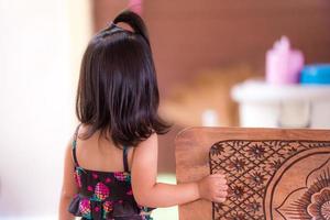 baksidan av den asiatiska söta lilla flickan med svart axellangt hår. ett barn i svart baddräkt väntade på sin mamma framför huset. barnet är 3 år. foto