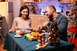 Lycklig familj Sammanträde på dining tabell i xmas dekorerad kök fira jul Semester. romantisk glad par äter xmas middag njuter utgifterna vinter- säsong tillsammans foto