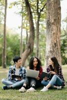 tre ung högskola studenter är läsning en bok medan avkopplande Sammanträde på gräs i en campus parkera med henne vänner. utbildning begrepp foto