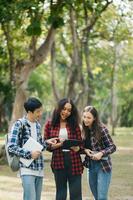 tre ung högskola studenter är läsning en bok medan avkopplande Sammanträde på gräs i en campus parkera med henne vänner. utbildning begrepp foto