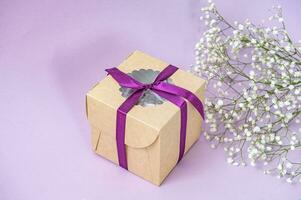 gåva hantverk låda med band på lila bakgrund med små vit Gypsophila blommor foto
