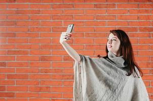 vacker tjej i grå tröja som gör selfie med smartphone, leende glatt foto