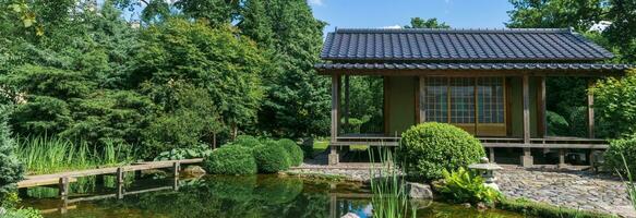 japansk trädgård med en damm, sicksack- bro, sten lykta och en te hus foto