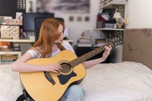 ung kvinna som spelar akustisk gitarr hemma foto