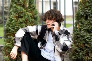 ung man talande på de telefon medan Sammanträde i de parkera foto