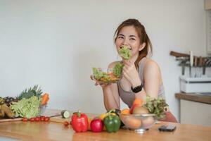 ung atletisk kvinna är framställning en friska organisk vegetabiliska sallad i en modern kök på Hem. foto