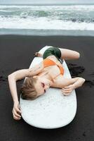 kvinna surfare är liggande på surfingbräda på svart sandig strand. med henne ögon stängd och i avslappnad utgör foto