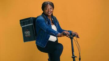 ung och aktiva kurir använder sig av modern cykel till leverera paket med precision till de stad kontor. afrikansk amerikan lady med ryggsäck arbetssätt som professionell leverans person. foto