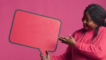 afrikansk amerikan skönhet innehav en röd Tal bubbla attrapp för text meddelanden och anteckningar i henne rätt hand. svart lady nickar i avtal med de innehåll av de ordbubbla copy mall. foto