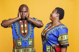 Make beläggning öron med händer och ignorerar fru talande. afrikansk amerikan par bär etnisk kläder har kommunikation problem och missförstånd i relation porträtt foto