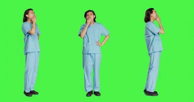 sjukvård anställd gapande på kamera över full kropp grönskärm, känsla trött efter svår natt flytta. asiatisk sjuksköterska medicinsk arbetstagare varelse sömnig och utmattad i studio, specialist. foto