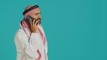 muslim vuxen tar inkommande telefon ring upp på mobil grej, kommunicerar avlägset på telefon linje. ung man representerar islamic kultur med Kläder, svar smartphone chatt. foto