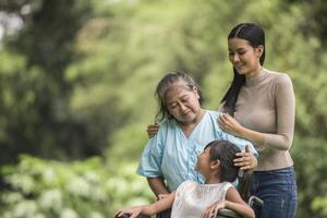 glad mormor i rullstol med sin dotter och barnbarn i en park, lyckligt liv lycklig tid. foto