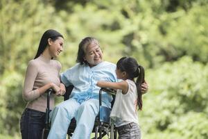 glad mormor i rullstol med sin dotter och barnbarn i en park, lyckligt liv lycklig tid. foto