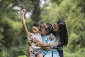 glad mormor i rullstol med sin dotter och barnbarn i en park, lyckligt liv lycklig tid. foto