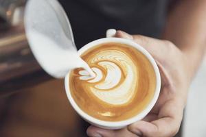 barista som gör latte- eller cappuccinokonst med skummande skum, kaffekopp i café. foto