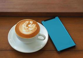 mobiltelefon tom skärm med cappuccino kaffe på träbord i kafé. mockup -reklam. foto