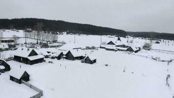 snöig fågelöga se. klämma. en vit by i de snö med små trä- hus och Nästa till den en stor skog med lång träd foto