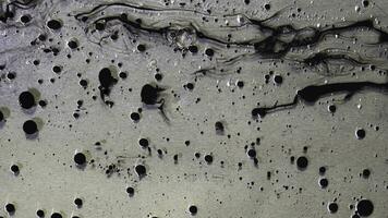 topp se av svart bläck droppar strömmande i flytande olja på metallisk, grå bakgrund. svart bollar av måla flytande på de oljig ämne yta. foto