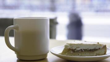 närbild av vit råna och tallrik med cheesecake. morgon- frukost med kaffe och klassisk cheesecake på trä- tabell. ljuv frukost i Kafé på bakgrund av fönster med upptagen gata foto