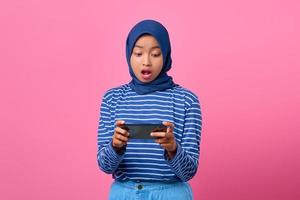 porträtt av chockad ung asiatisk kvinna som spelar videospel i mobiltelefon foto