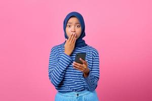 porträtt av chockad ung asiatisk kvinna som håller smartphone och täcker munnen med handen