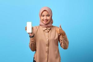 porträtt av leende ung asiatisk kvinna som visar smartphone tom skärm och gör tummen upp tecken