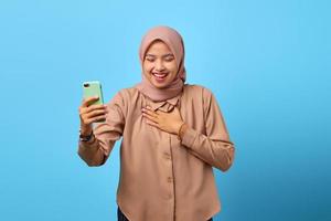 porträtt av lycka ung asiatisk kvinna som använder mobiltelefon med en annan hand på bröstet foto