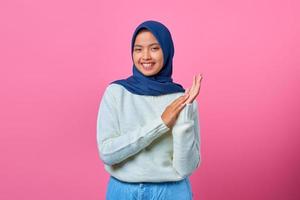 porträtt av leende ung asiatisk kvinna som visar klappande gest på rosa bakgrund