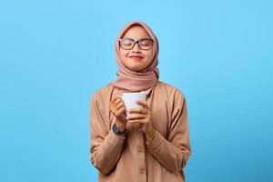 porträtt av lycka ung asiatisk kvinna hand hålla mugg över blå bakgrund foto