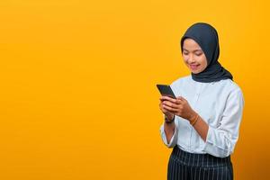 attraktiv ung asiatisk kvinna som använder en mobiltelefon och ser smartphone -skärmen på gul bakgrund foto