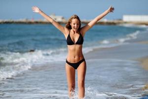 ung blond kvinna med vacker kropp i badkläder på en tropisk strand med öppna armar. foto