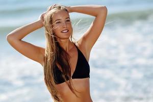 ung blond kvinna med vacker kropp i badkläder på en tropisk strand.