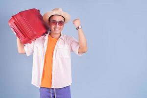 ung asiatisk man som håller röd resväska på blå bakgrund foto