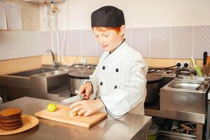 barn pojke i kockens kostym förbereder choklad pannkakor i kök i Kafé. skivor frukt, kiwi foto