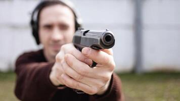 en man är siktar för en pistol. en man bär skyddande hörlurar. utomhus- däck skytte räckvidd. hobby. skjutvapen mot de vit vägg foto