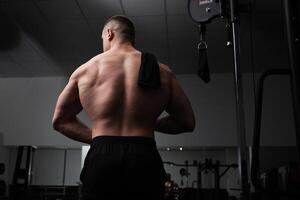 porträtt av en skön manlig idrottare kroppsbyggare i Gym, låg nyckel, mörker. poserar, tränare. kraft, styrka, abstraktion bakgrund foto