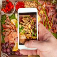 en man tar bilder av mat på hans telefon. räka, mellanmål, frukt, kött, grönsaker. en bild av mat på din telefon skärm. foto