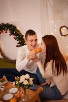 en ung Lycklig par i kärlek äter i en Foto studio. de kille och de flicka är rolig matning varje Övrig. Framställ för modeller i en studio för jul familj middag för ny år afton, frukost i säng