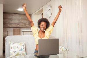 en afrikansk amerikan kvinna frilansare, arbete från Hem. kvinna i främre av bärbar dator är Lycklig, leende. vinnande lotteri, anlitade, lager ha uppstått, kryptovaluta har vuxen, Bra Nyheter. händer upp foto