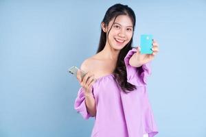 ung asiatisk tjej som använder smartphone på blå bakgrund foto