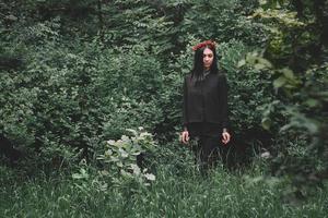 vacker tjej med ögonen stängda i svarta kläder och röda örhängen på bakgrunden av skogen foto