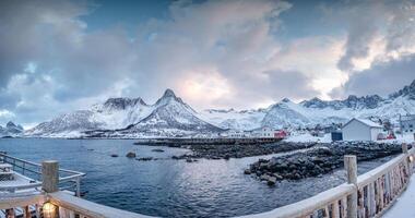 scandinavian by med snö täckt berg räckvidd på kustlinje i vinter- på mefjord brygge, senja ö foto