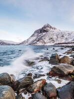 havslandskapsvåg som slår mot stenar med berg på den arktiska kusten foto