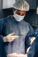 fokuserade kirurg håller på med en kirurgi. porträtt av en hälsa vård arbetstagare bär en mask. foto