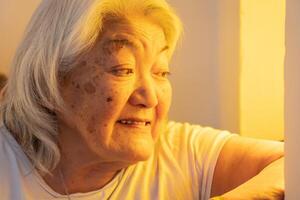 senior vuxen kvinna ser ut de fönster och leende. ljus miljö. foto