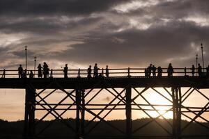 silhuett turister resa gående på trä- mån bro foto
